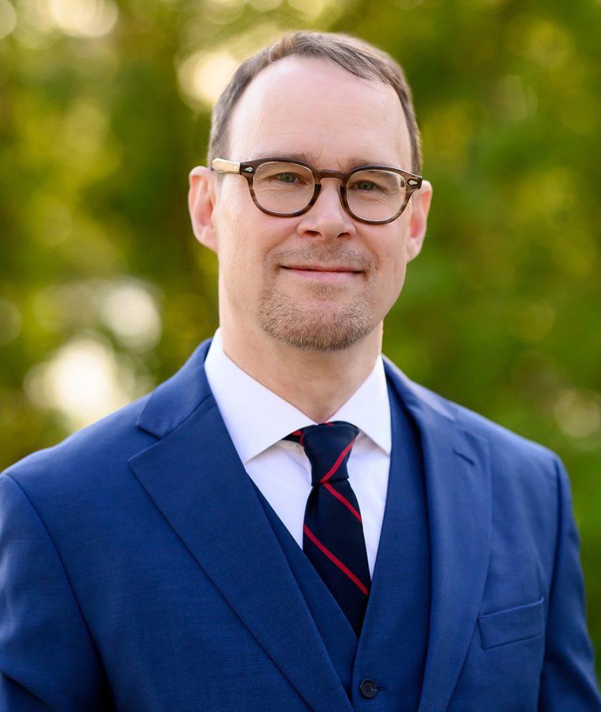 Jamie McLennan, président de l'ATIM, fait face à la caméra en portant un costume bleu et une cravate.